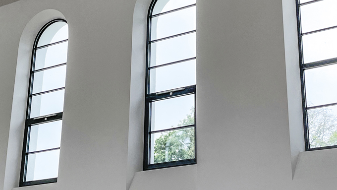 Drei Bogenfenster in einem minimalistischen Interieur, die natürliches Licht hereinlassen und von sauberen weißen Wänden und einer strukturierten Decke eingerahmt werden.