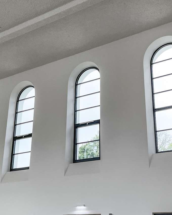 Drei Bogenfenster in einem minimalistischen Interieur, die natürliches Licht hereinlassen und von sauberen weißen Wänden und einer strukturierten Decke eingerahmt werden.