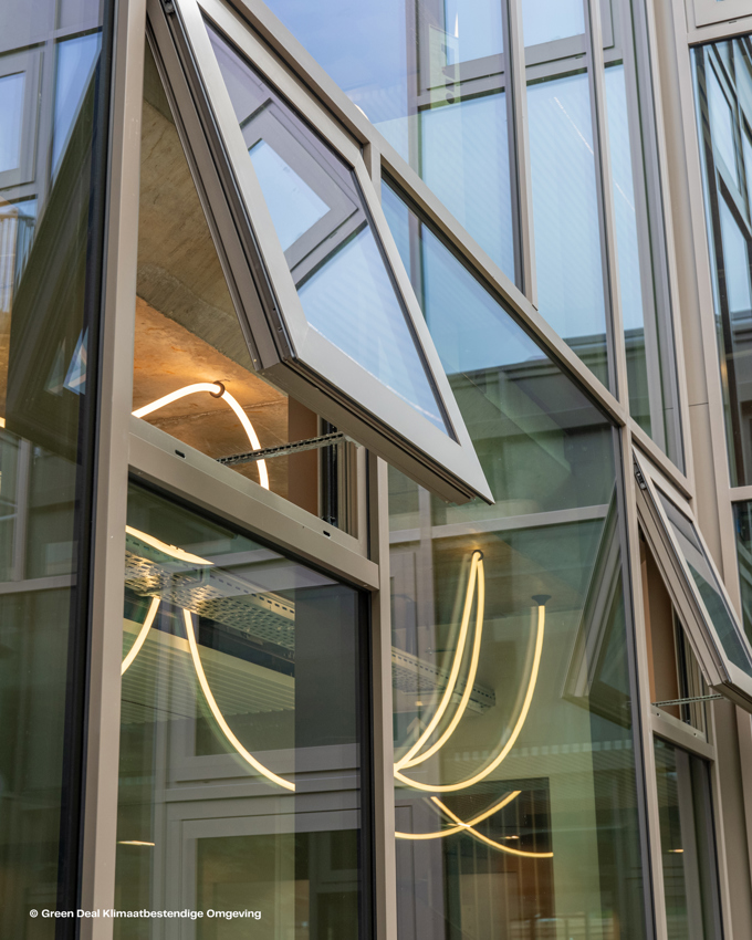 Moderne Gebäudefassade mit eckigen Glasfenstern, von denen einige offen sind, Neonlicht reflektieren und zeitgenössisches architektonisches Design präsentieren.